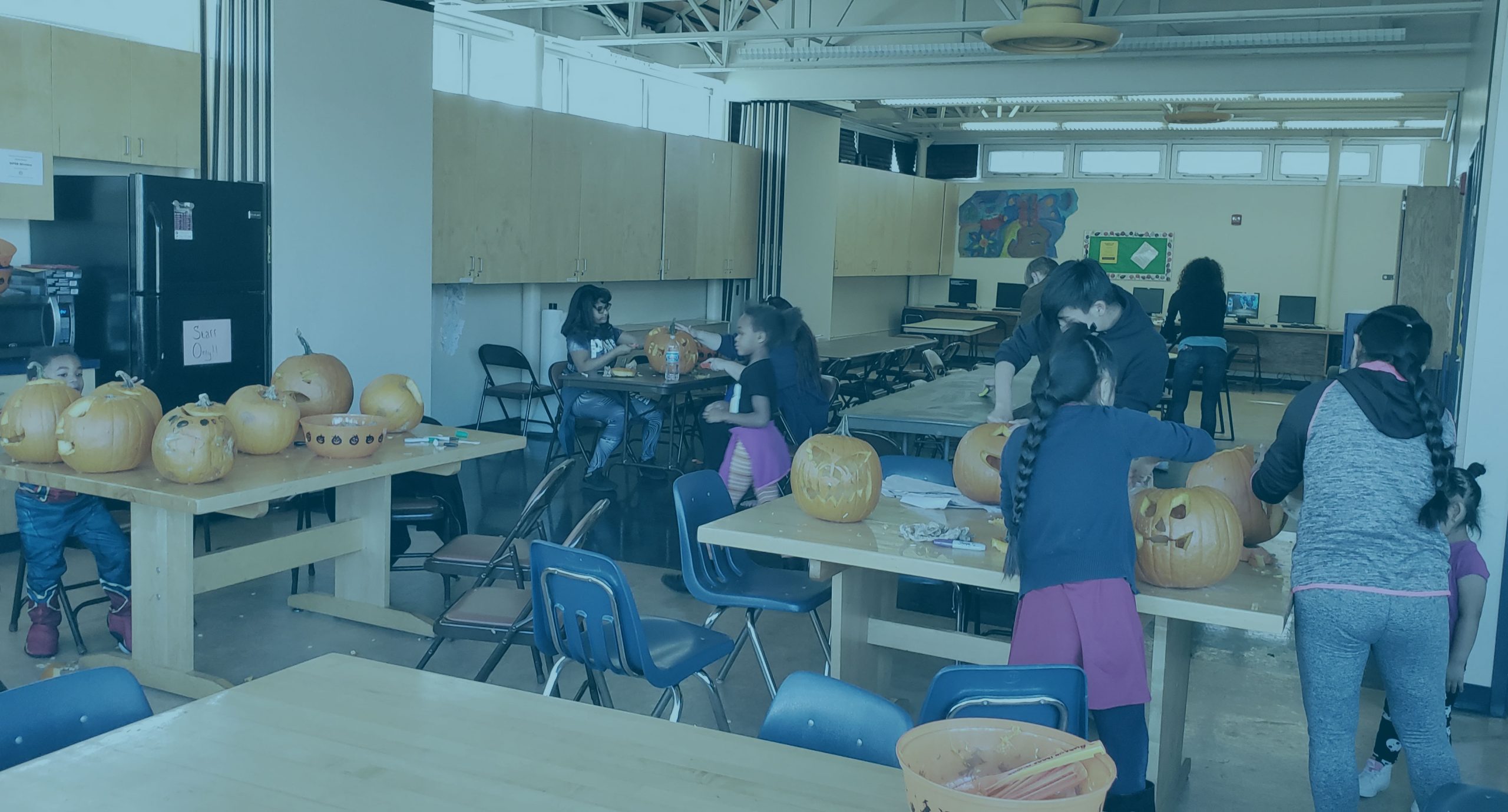 Students in a classroom carving pumpkins, with a dark light blue overlay